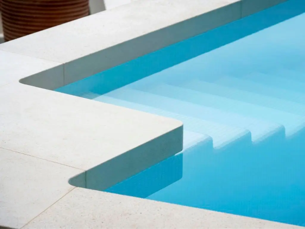 Close-up of smooth light-colored pool coping over the pool steps