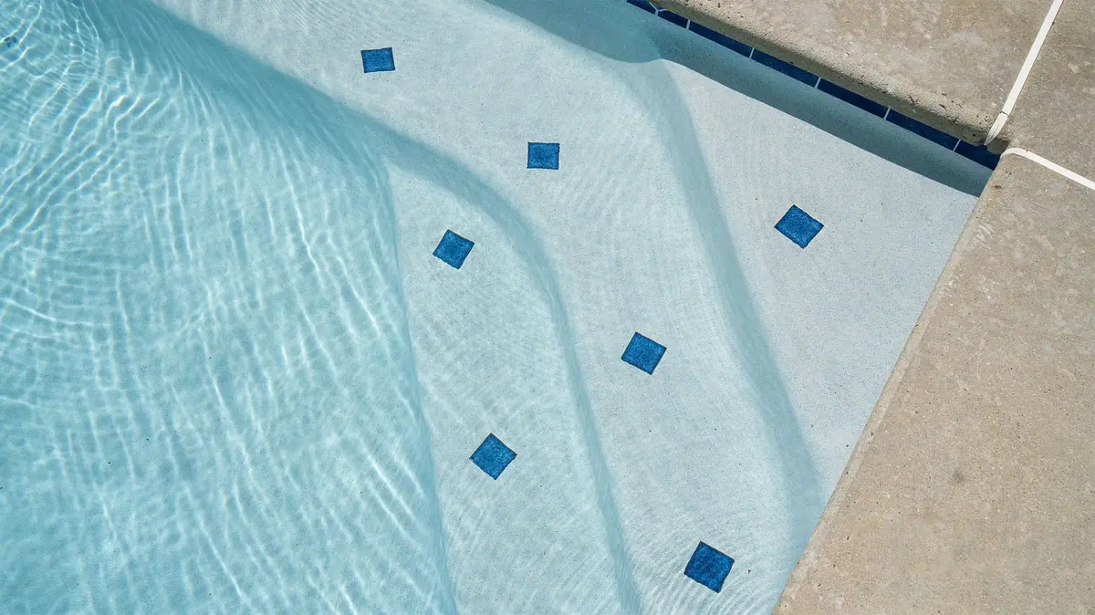 Close-up of white quartz pool finish on steps with small blue accent tiles