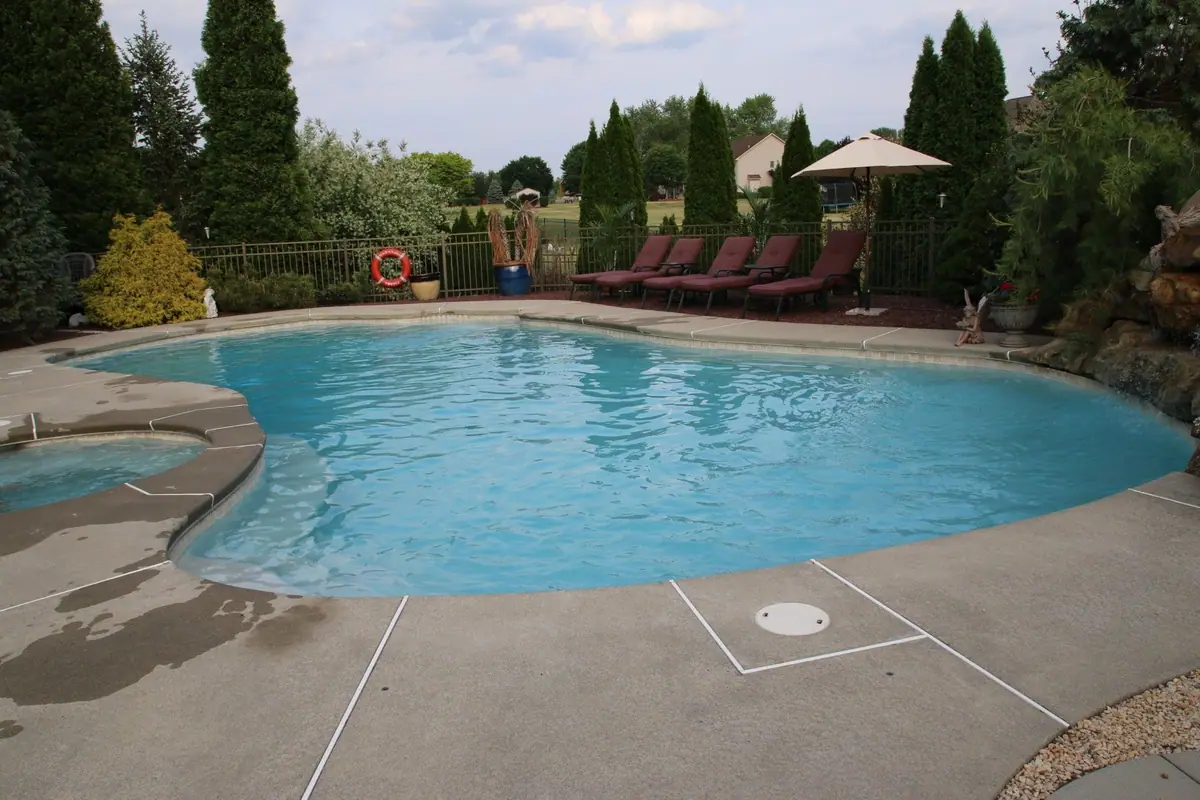 Free-form residential pool with attached spa and concrete deck