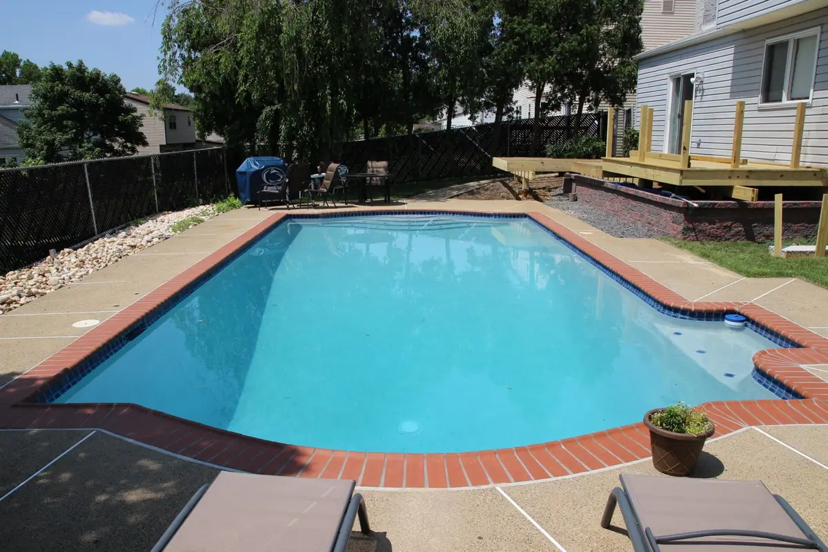 Wide view of a rectangular pool with white plaster finish, brick coping and wood deck